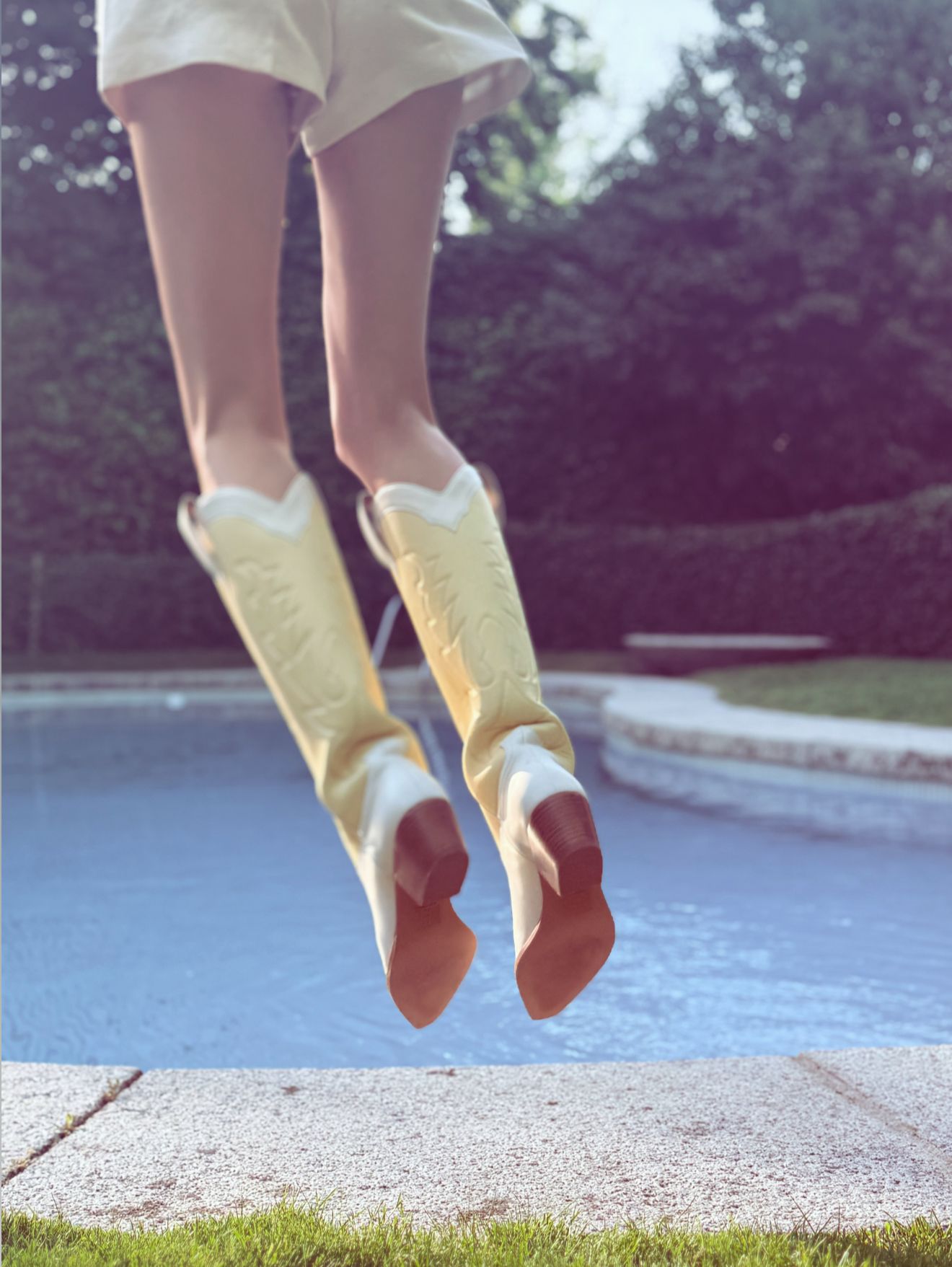 Person wearing yellow and white cowboy boots jumping into a pool with a blurred background.
