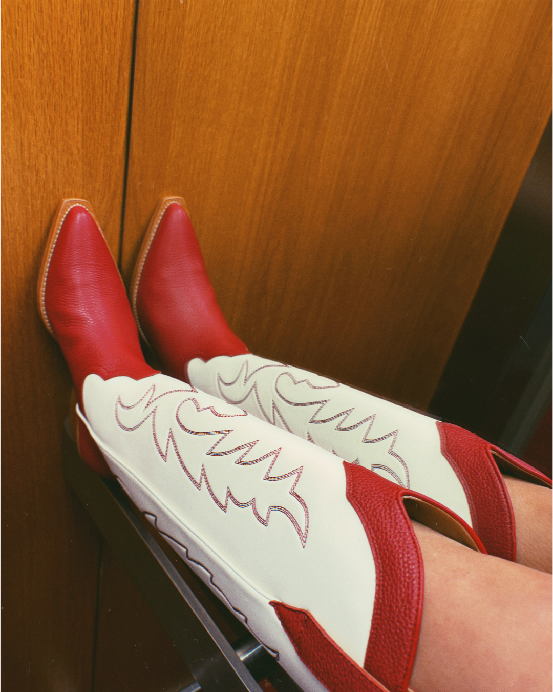 Red and white cowboy boots with red embroidery in a wooden panelled lift.