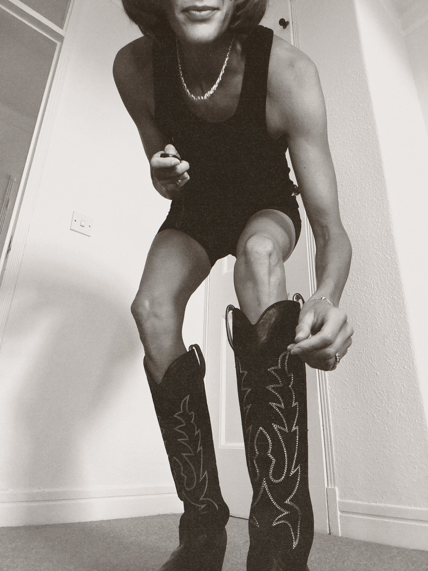 Person wearing a black outfit and cowboy boots indoors.