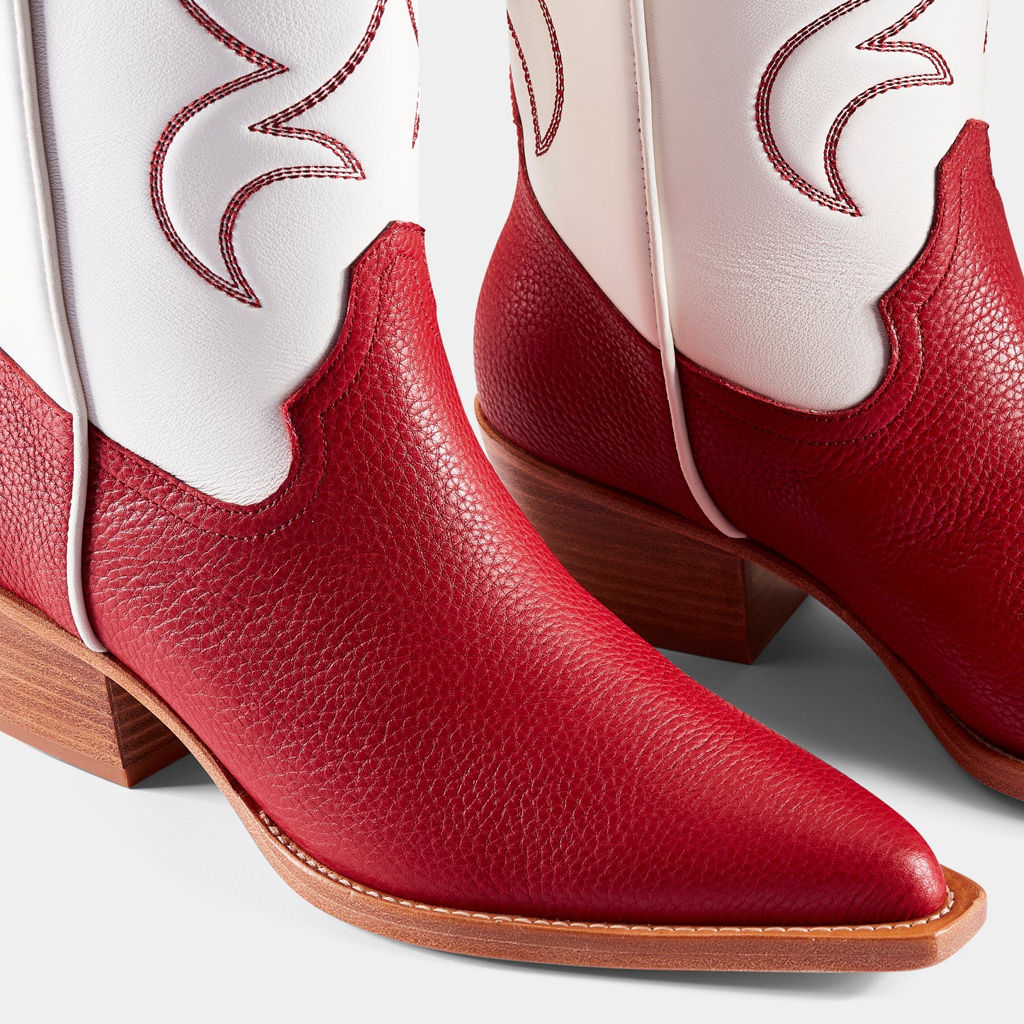 A red and white embroidered cowboy boot with a pointed toe and side pull tabs - close up.