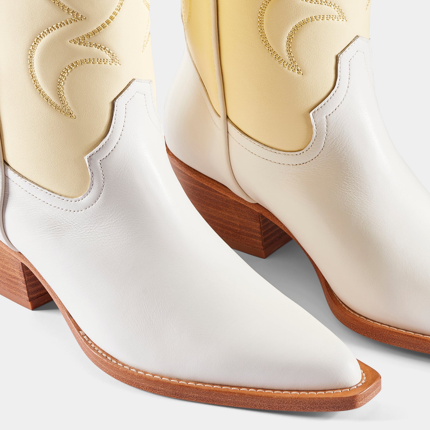 A pair of white and yellow embroidered cowboy boots with a pointed toe and low heel - upclose.
