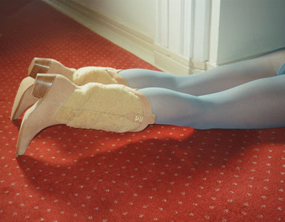 Person lying on red carpet wearing tan suede and shearling cowboy boots.