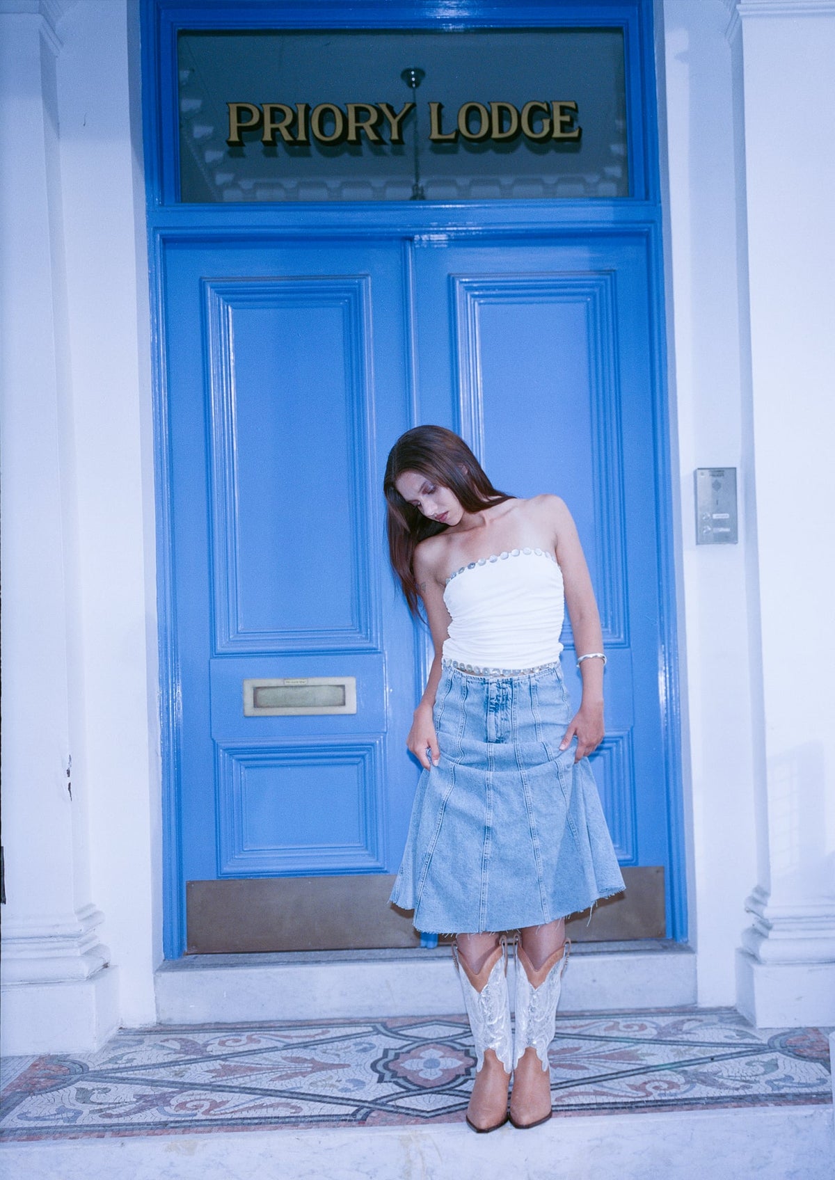 Woman in silver and tan cowboy boots standing in front of a blue door with 'Priory Lodge' sign