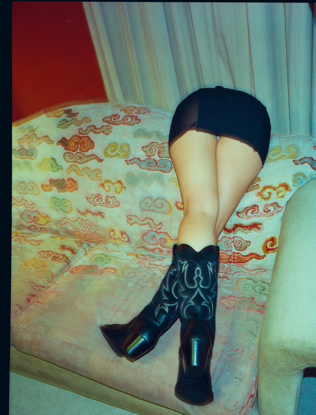 Person wearing black mini skirt and black cowboy boots on a Tibetan cloud printed sofa
