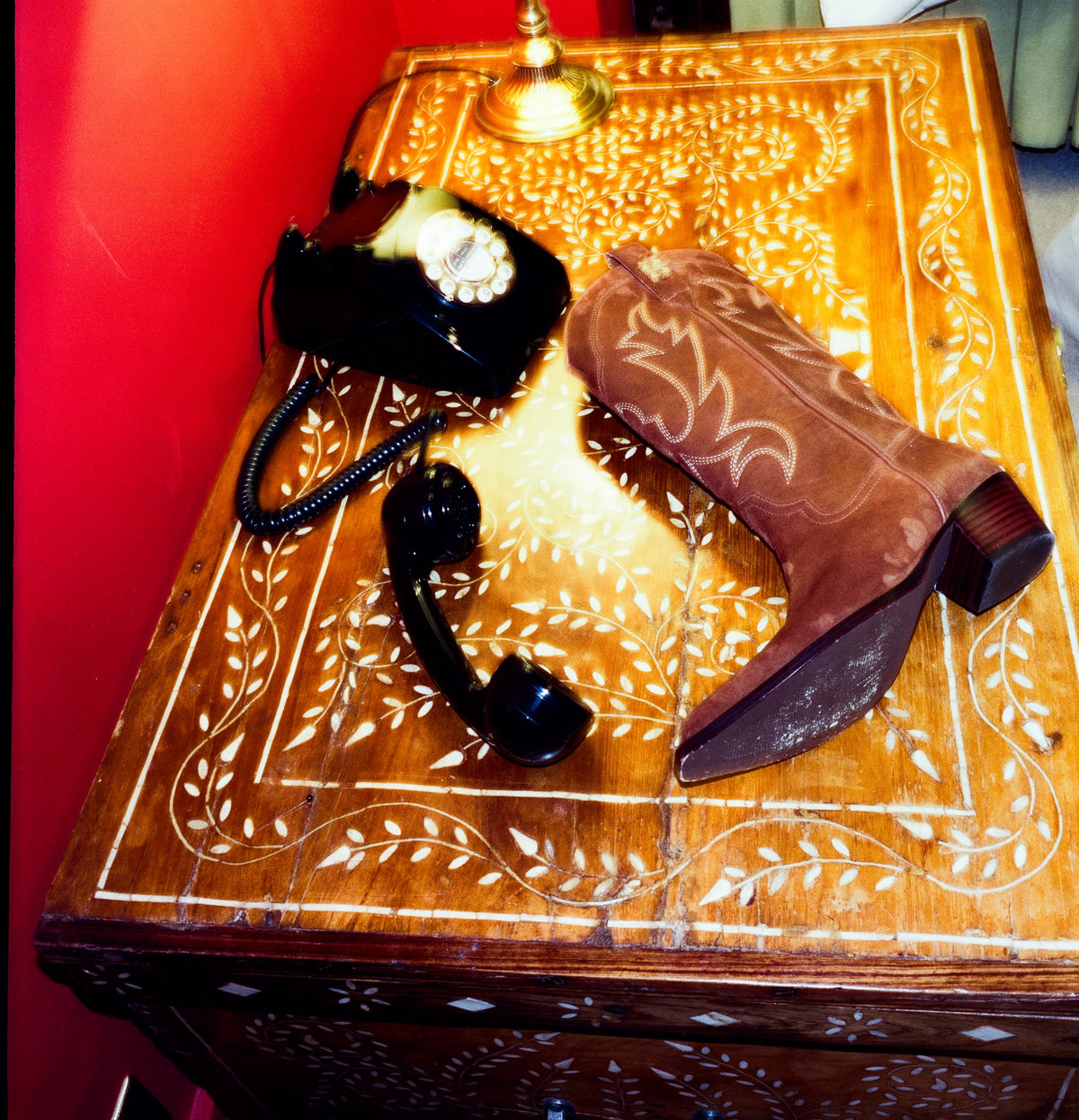 Still life of cognac brown cowboy boot on Moroccan chest with vintage telephone