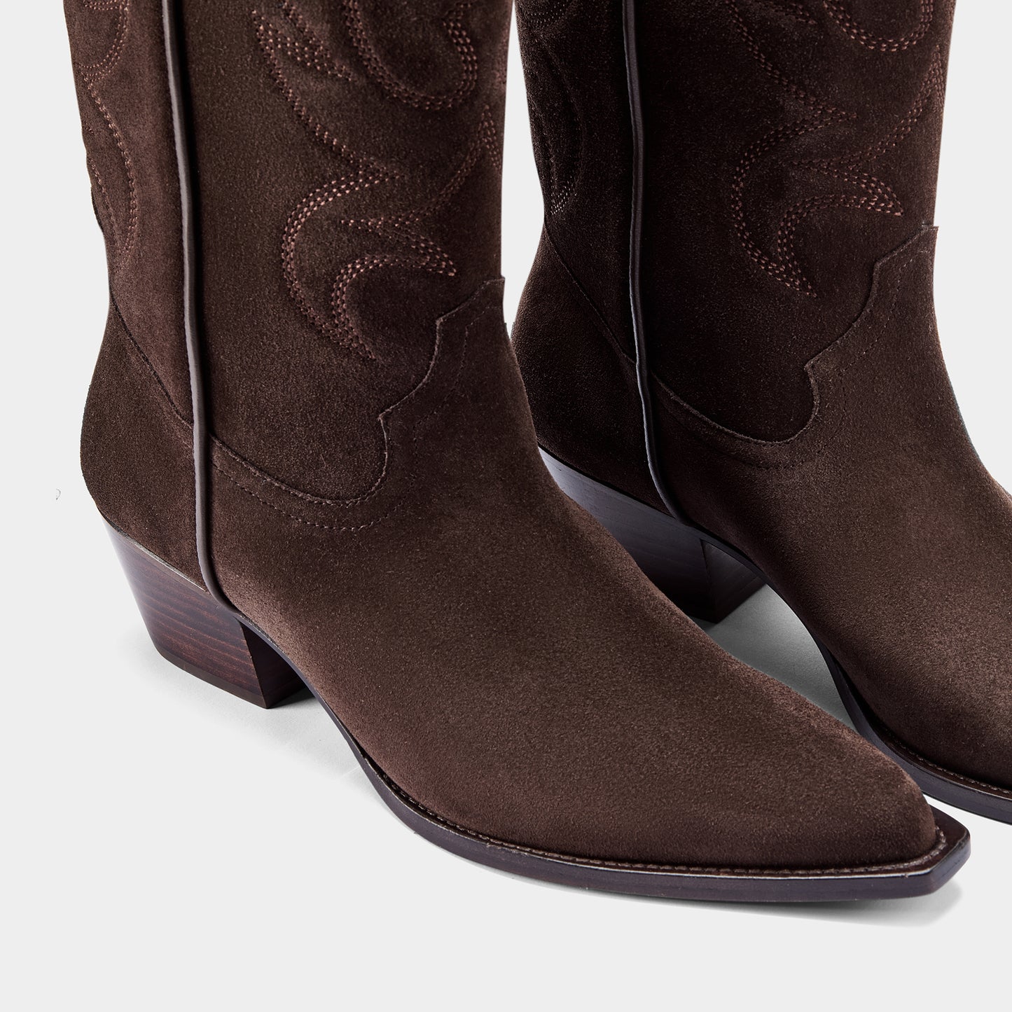 Chocolate brown cowboy boot with logo hardware on a light grey background.