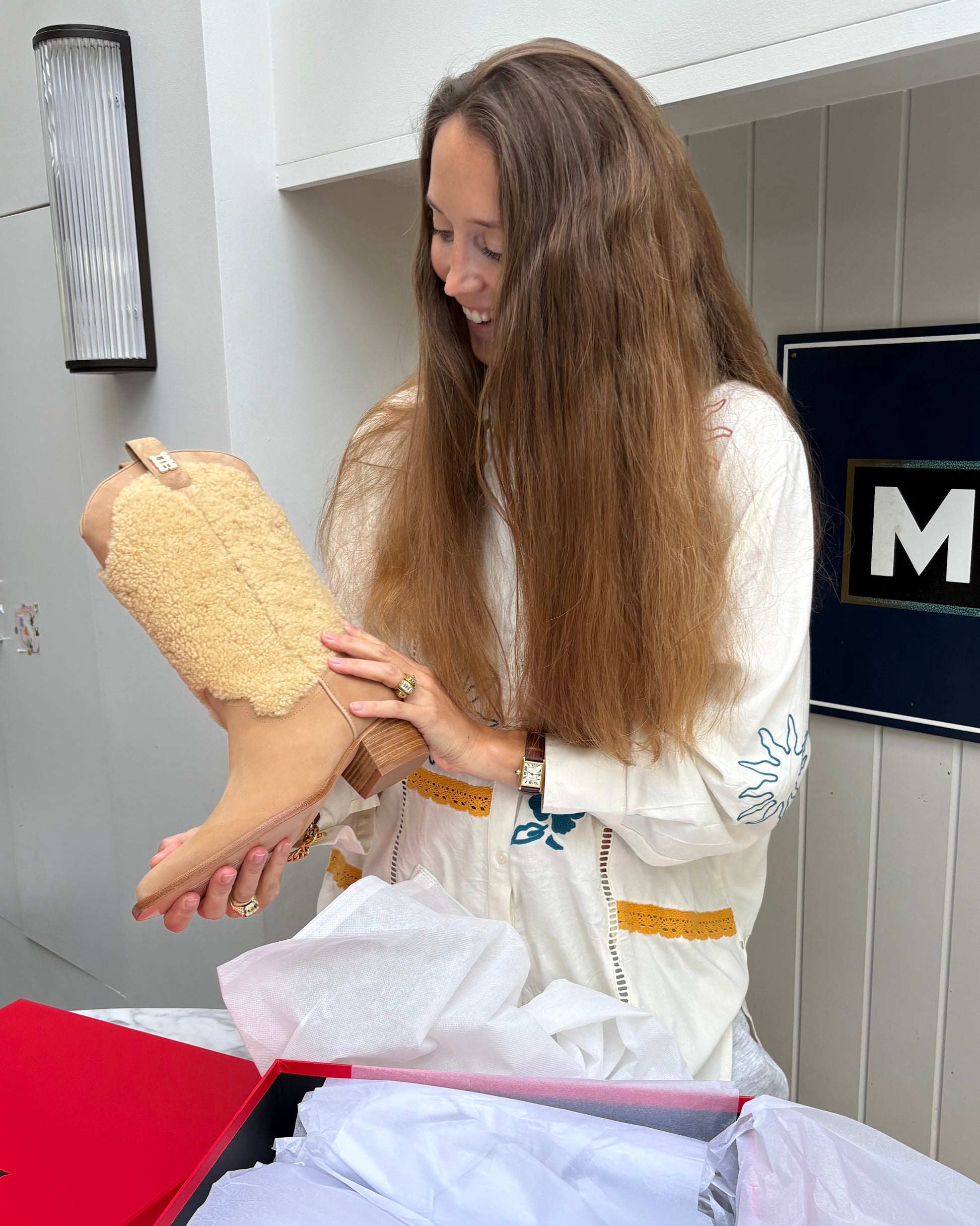 Vita holding a tan suede and shearling cowboy boots in the kitchen