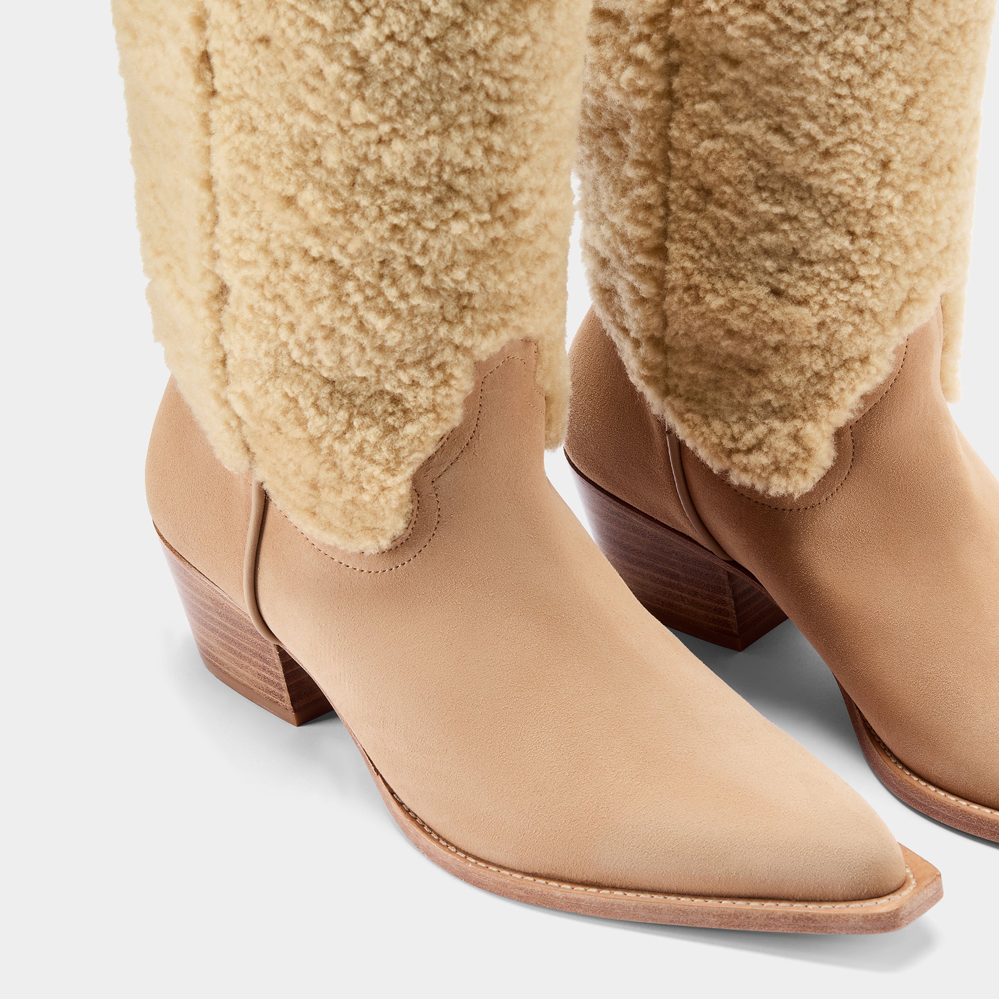 Tan suede cowboy boot with shearling shaft on a light grey background - close up.