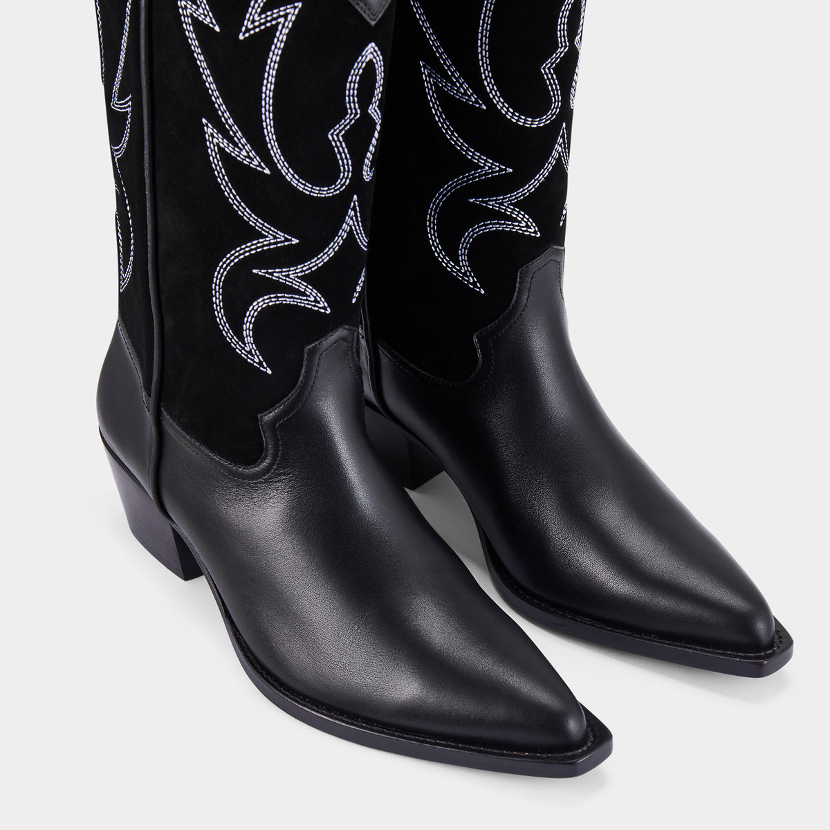Black cowboy boots with white embroidery on a light grey background - close up