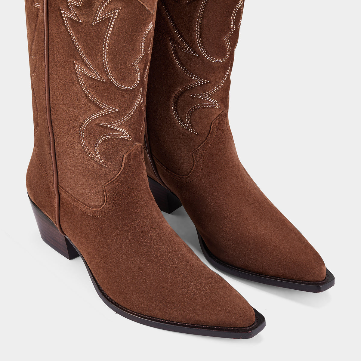 Cognac suede cowboy boot with embroidery detail on a white background - close up