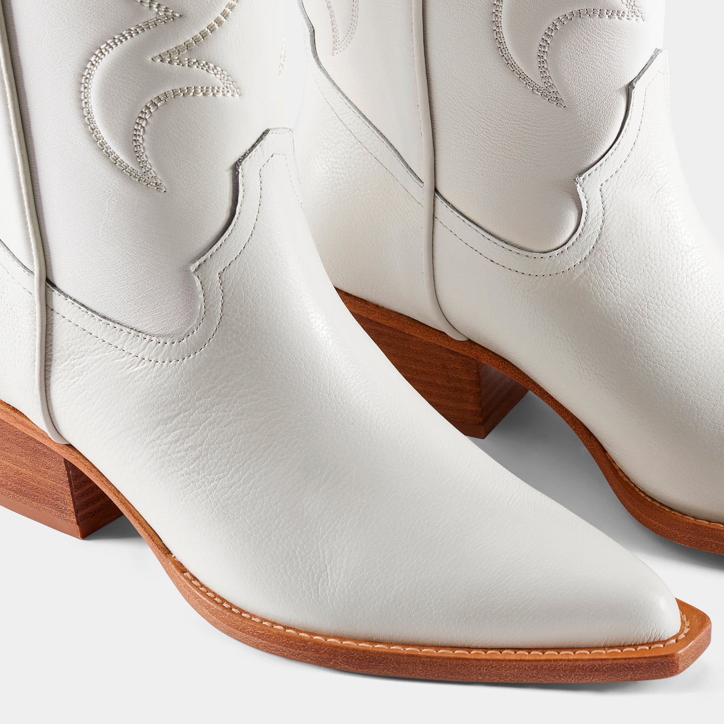 A white leather cowboy boot with embroidered details and a low heel - close up.