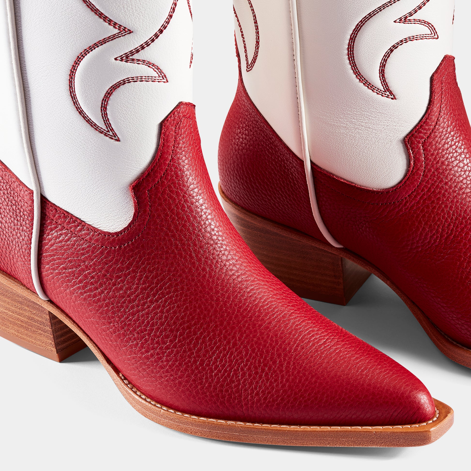 A red and white embroidered cowboy boot with a pointed toe and side pull tabs - close up.