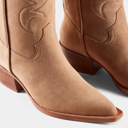 A tan-coloured suede cowboy boot with embroidered panels, a pointed toe, and a low heel - close up.
