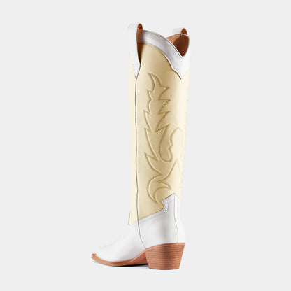 A pair of white and yellow embroidered cowboy boots with a pointed toe and low heel - back angle.