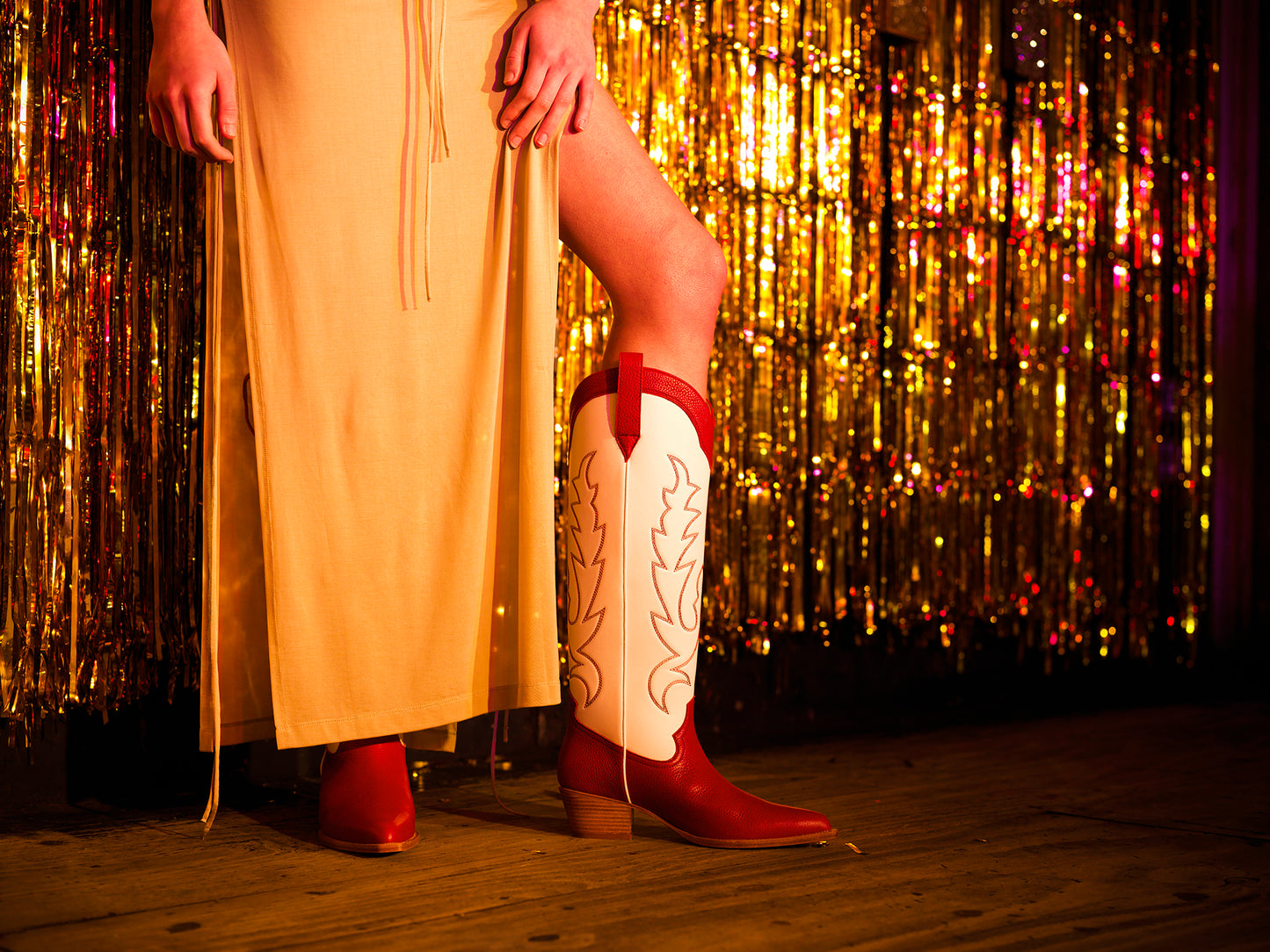Model on stage with gold tinsel curtain wearing red and white cowboy boots.