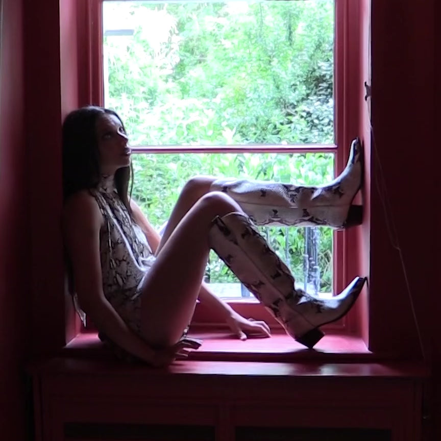 Video of the Duke's Original Tall in Snake Eyes python-print calf nappa cowboy boot, model sitting in a window wearing a snake print silk outfit